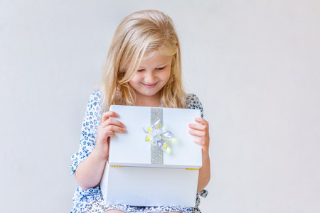 A blonde 6 year old girl looks with interest into the box with a giftの写真素材