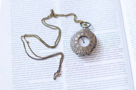 A round watch with a chain is lying on an open magazine.の写真素材