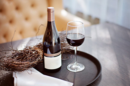 A bottle of red wine and a full glass on a tray stand on a table in the restaurant. Empty label template.の写真素材