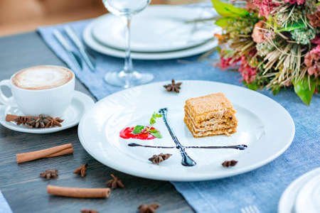 A piece of honey cake on a large white plate, decorated with chocolate syrup, mint. Restaurant menuの写真素材