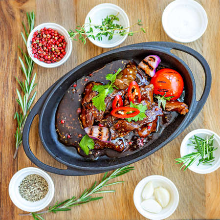 Roast meat with baked tomatoes and onions with sweet sauce, beautifully served in cast-iron dishes. Restaurant menuの写真素材
