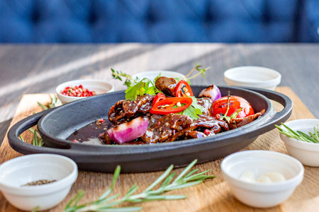 Roast meat with baked tomatoes and onions with sweet sauce, beautifully served in cast-iron dishes. Restaurant menuの写真素材