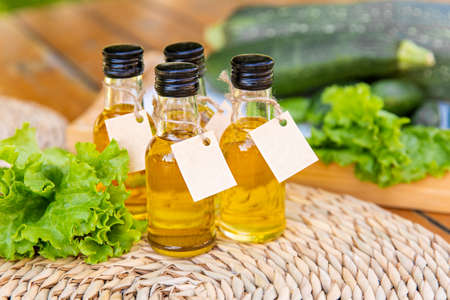 Four types of vegetable oil in small bottles with cardboard labels on the background of salad leaves, zucchini and cucumbers. The concept of healthy healthy food.の写真素材