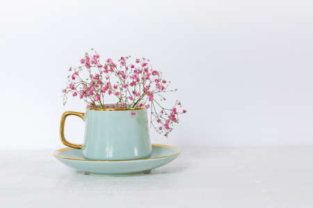 Turquoise cup with beautiful pink gypsophila flowers on a light background, minimalism, copying space. Gift card, a concept of the mood of a spring or summer morningの写真素材