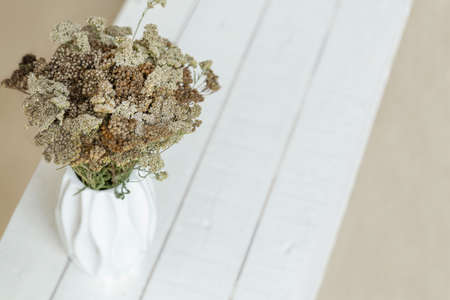 Bouquet of white, brown, beige dried flowers in a white vase on a white wooden background. Card, Interior decor.の写真素材