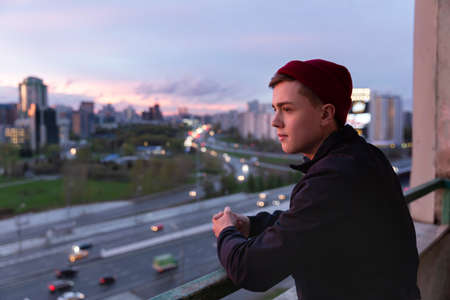 A young man thoughtfully observes the life of the city from the height of the observation deck. Sunset sunlight. the real life of youth.の写真素材