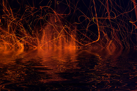 Flames of fire and sparks on a black background with reflection in water
