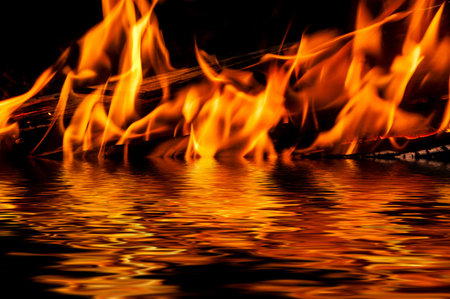 Flames of fire and sparks on a black background with reflection in waterの写真素材