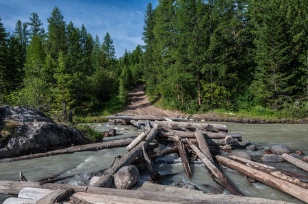Ruined wooden bridge across the river on a background a forest and blue sky in the mountainsの写真素材