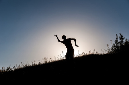Silhouette of a slender young man making figures in the rays of the sun on the hillside. He's young, fun, free and happy.の写真素材