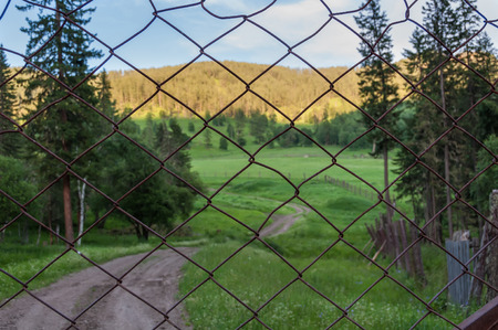 Scenic view of a rural road, meadows and mountains through a steel mesh fenceの写真素材