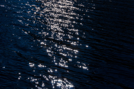 Abstract decorative background of solar glare and the tracks on the dark water from sunlightの写真素材