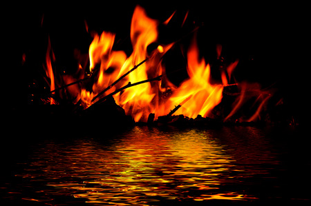 The flames from the fire on a black background with reflection in waterの写真素材