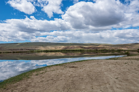 Beautiful landscape with reflections of blue sky and clouds in the lake. A small lake in the steppe, sunny summer day.の写真素材