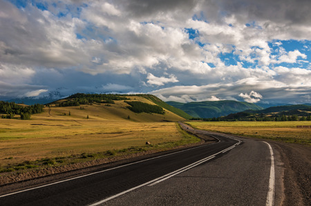Evening landscape with a road in the steppe, the mountains on the horizon, cloudy sky and evening lighting.の写真素材