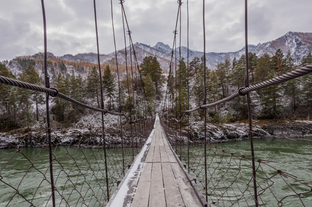 Suspension footbridge over the river in winter in mountainsの写真素材