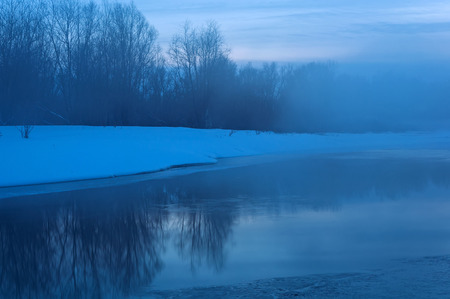 Night landscape with the river, partially covered with ice, snow on the shore and the mist over the water, shot long exposureの写真素材