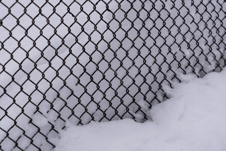 Steel mesh fence against the white snow in winterの写真素材