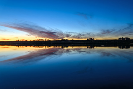The picturesque orange and brown sunset on the lake with beautiful delicate clouds reflecting in waterの写真素材