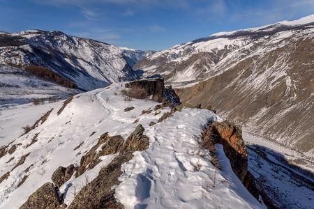 The picturesque top view on the mountains covered with snow, cliffs and the valley between the mountains in the canyon on a background of blue sky and clouds in winterの写真素材