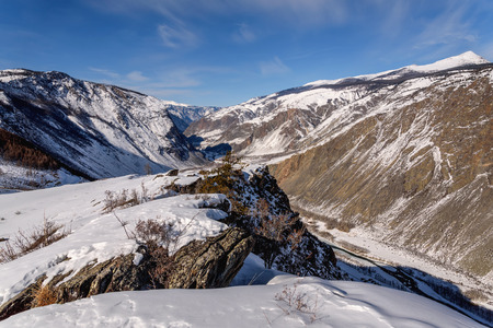 The picturesque top view on the mountains covered with snow, cliffs and the valley between the mountains in the canyon on a background of blue sky and clouds in winterの写真素材