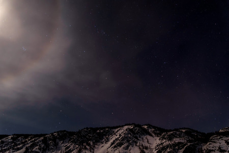 Beautiful winter night landscape with mountains covered with snow and a part of the lunar halo against a background of stars and dark skyの写真素材