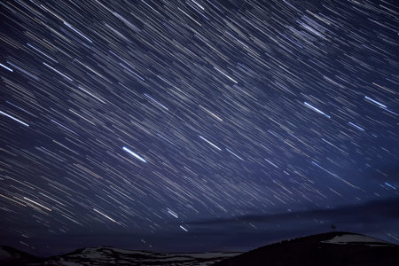 Beautiful night landscape with traces of stars in the night sky and clouds on a background of...