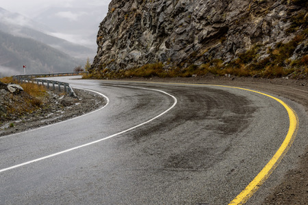 Scenic view of the hairpin bend wet winding road through the pass, part of the mountain serpentine in autumn cloudy weather with fogの写真素材
