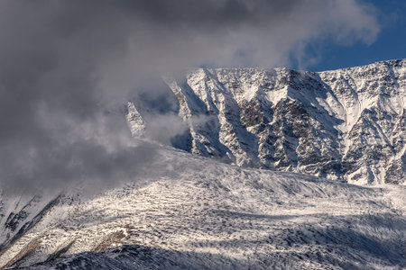 Scenic abstract background with a relief of mountains covered with snow closeup and fluffy clouds