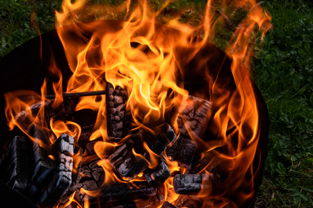 Red and orange flame of a bonfire and black pressed coal in brazier for barbecue on grass backgroundの写真素材