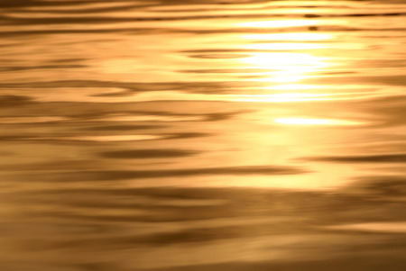 Golden background of water texture with sun reflection and beautiful soft waves at sunsetの写真素材
