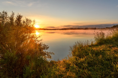Amazing golden sunrise on the lake with sun, clouds, grass in the foreground and reflections