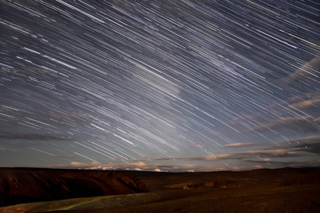 Amazing night landscape with the movement of stars in the form of tracks and clouds in the sky over...