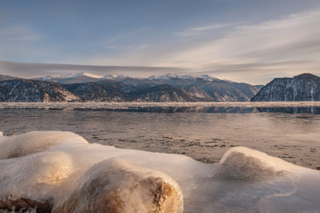 Beautiful winter landscape with a lake, ice on the water and the shore, snowy mountains and...