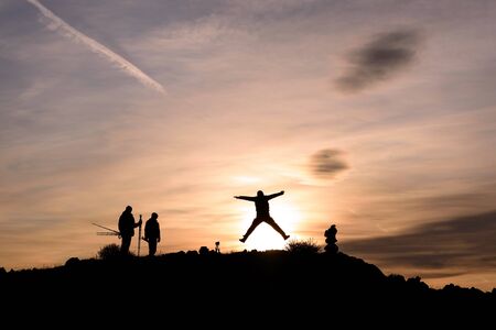 Silhouettes of people on the side of a mountain in the sunlight at sunrise against a blue sky with cloudsの写真素材