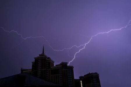 Colorful flash of lightning against the dark night sky above the roof of a building with a spire...