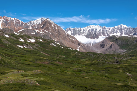 Amazing summer landscape with a valley and hills covered with green dwarf birch, snowy mountains and a glacier against a blue sky and clouds. Altai, Russiaの写真素材