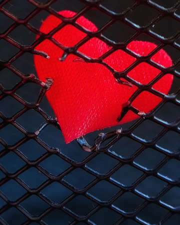 red heart breaks free through a metal grate. macro. a photoの写真素材
