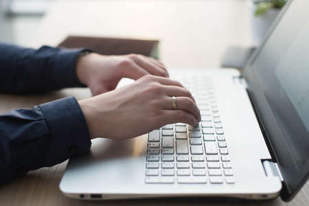 Hands typing on a laptop keyboard. A man works in an office at his workplace.の写真素材
