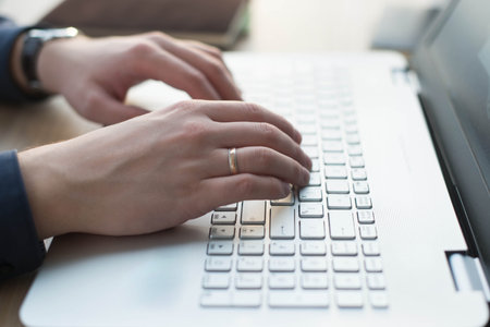 Hands typing on a laptop keyboard. A man works in an office at his workplace.