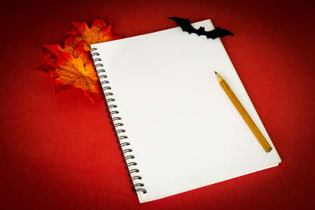 Halloween notepad on a red background. Pencil, blank notepaper, and a bat. Blank for an invitation to halloween. Copy space. Flatlay.の写真素材