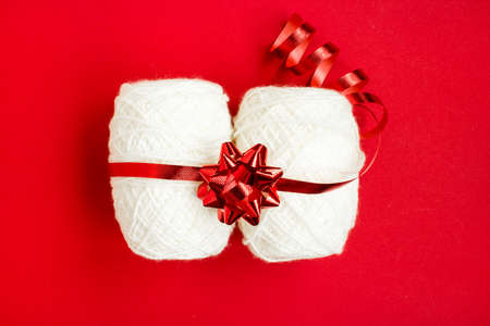A ball of white thread in a festive package on a red background. The concept of Christmas gifts for needlewomen. Copy space. Top view.の写真素材