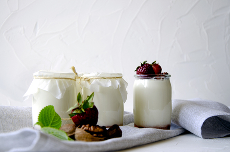 Homemade yogurt with fresh strawberries. Ingredients for a healthy breakfast are halves of strawberries, walnuts and yogurt with glasses on textiles on a white concrete background.の写真素材