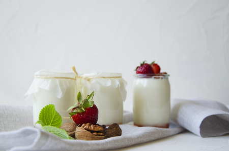Homemade yogurt with fresh strawberries. Ingredients for a healthy breakfast are halves of strawberries, walnuts and yogurt with glasses on textiles on a white concrete background.の写真素材