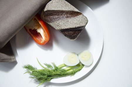 Healthy tasty loaf of bread, a half of red pepper and sliced boiled egg on a white plate, closeup.の写真素材