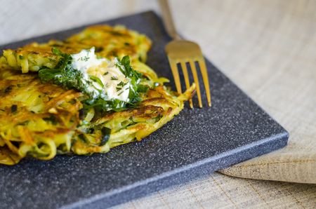Roesti. Potatoes grated with greens, fried in butter. Serve on a stone board with sour cream, garlic and greens. Served with textile napkin and cutlery. Vegetarian table. Horizontal. Copy space.の写真素材