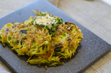 Roesti. Potatoes grated with greens, fried in butter. Serve on a stone board with sour cream, garlic and greens. Vegetarian table. Horizontal.の写真素材
