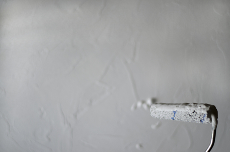 Closeup of wall painting using a roller. Paint is dripping from the bottom right corner. Coloring in white-gray color, concrete. Home repair, interior design. Rough finish.の写真素材