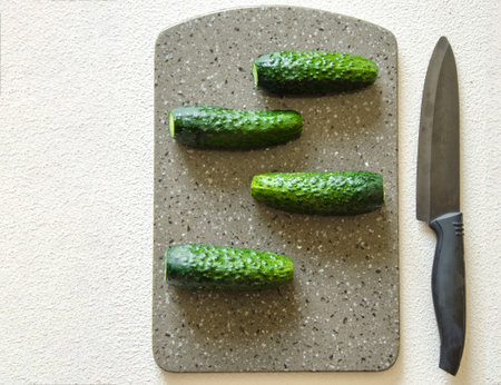 Cucumber on a stone plate. On a white background, four cucumbers lie on a stone board, a knife is...