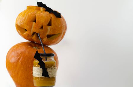 A glass of fresh pumpkin juice, decorated for Halloween with a flying bat, served with a straw pumpkin jack in the background. White background. Copy space.の写真素材